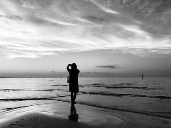 Rear view of silhouette woman standing on beach against sky