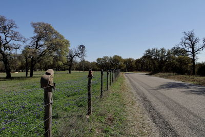 Road by trees on field against sky