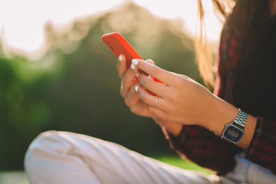 Midsection of woman using smart phone while sitting outdoors