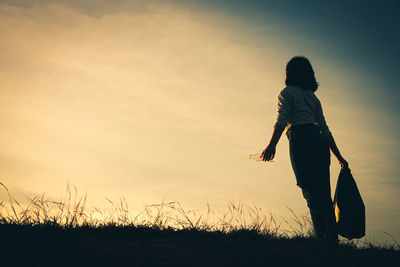 Rear view of woman walking on field against sky during sunset