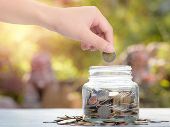 Cropped hand putting coin in jar on table