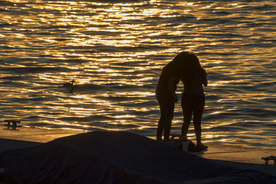 Silhouette women standing on pier by sea during sunset