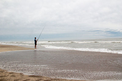 Man fishing at beach against sky