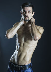 Shirtless young man with hands behind head standing against gray background