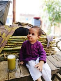 Boy looking away while having sugar cane juice on wooden bench