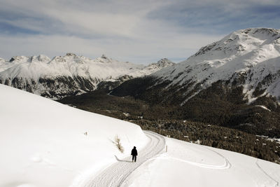 Rear view of person walking on snowcapped mountains against sky