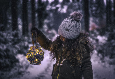 Girl in warm clothing holding illuminated lantern
