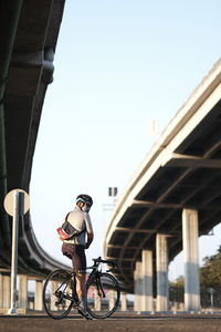 Man riding bicycle on bridge against sky