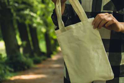 Close-up of unrecognizable female hand holding cotton eco bag in park. reusable eco bag in park