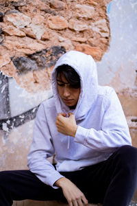 Man wearing hood sitting against wall