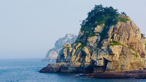 Rock formation by sea against clear sky