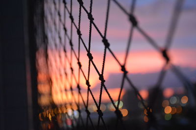 Close-up of chainlink fence against sky at sunset