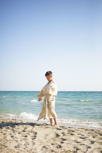 Rear view of woman standing at beach against clear sky