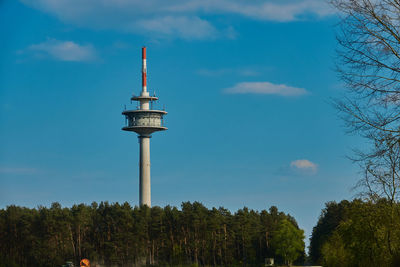 High television tower behind a forest in front of a blue sky