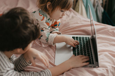 Little brother and sister lie in the bedroom on the bed and look at the laptop. high quality photo