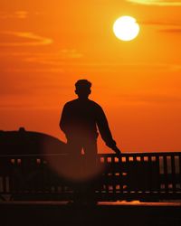 Silhouette man standing by railing against orange sky