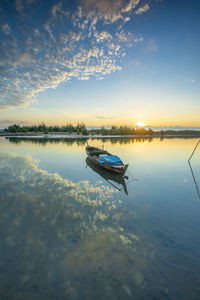 Boat moored in lake against sky during sunset