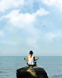 Full length of young woman sitting by sea