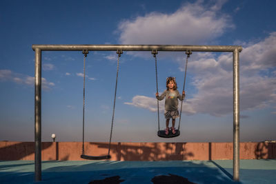 Young girl swings standing up on a playground at sunset