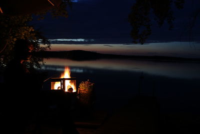 Silhouette trees by lake against sky at night