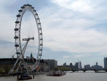 Ferris wheel in city against cloudy sky