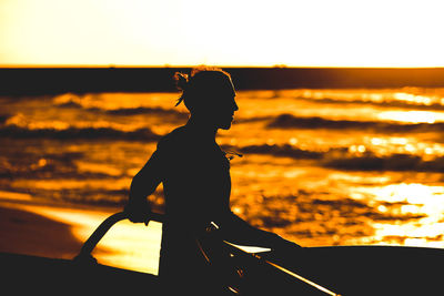 Silhouette man sitting on beach against sky during sunset