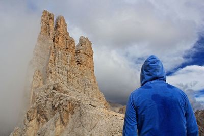 Rear view of man looking at rock formation against cloudy sky