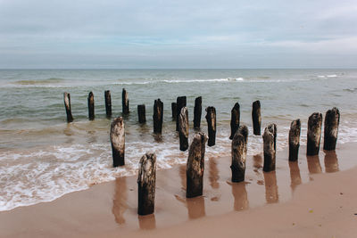 Wooden posts on beach against sky