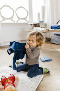 Cute girl holding clothes while sitting on floor at home