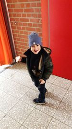 Full length portrait of boy standing against brick wall