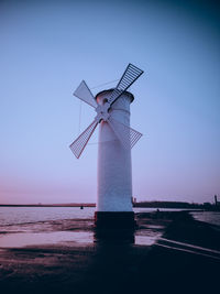 Lighthouse by sea against clear sky during sunset