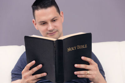 Portrait of man holding book against gray background