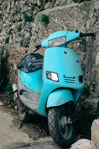 Abandoned motor scooter parked by stone wall