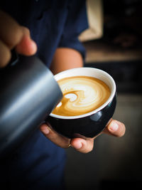 Midsection of person pouring milk in coffee