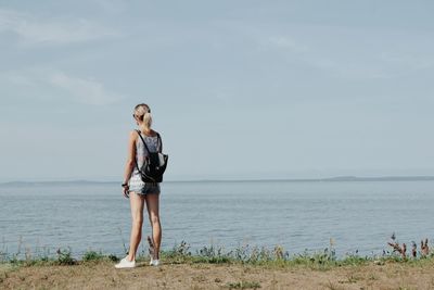 Full length of young woman standing on sea shore against sky