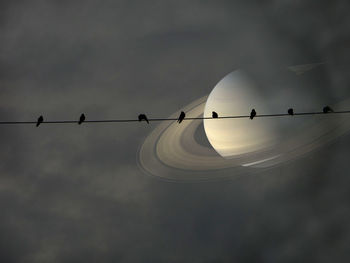 Low angle view of silhouette birds against saturn in cloudy sky