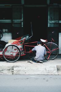 Rear view of man repairing bicycle on road