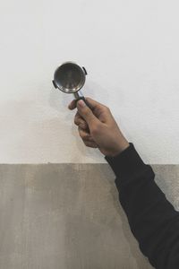Cropped hand of man holding coffee maker equipment by wall
