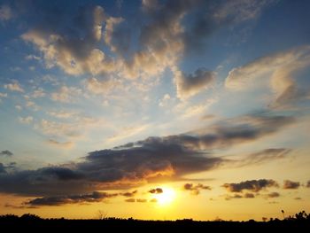 Low angle view of sun streaming through clouds during sunset