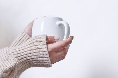 Female hand holding hot tea cup against white background. a woman in warm knitted sweater holds in