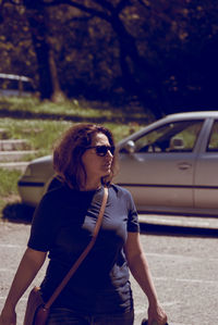 Woman looking away against car on sunny day