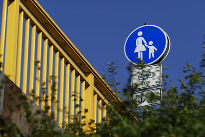 Low angle view of road sign against clear blue sky