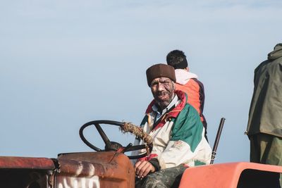 Men riding motorcycle sitting against sky