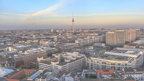 Fernsehturm amidst cityscape against sky during sunset