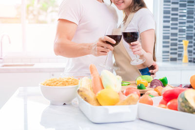 Midsection of young couple toasting wineglasses while standing by food in kitchen