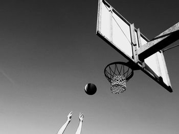 Cropped hands throwing ball in basketball hoop against sky