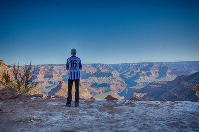 Rear view of man standing on landscape against blue sky