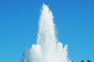 Low angle view of splashing fountain against clear blue sky