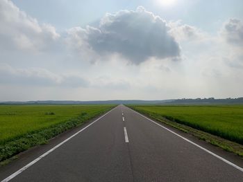 Empty road amidst field against sky