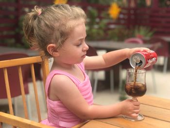 Girl pouring soda from can in glass while sitting on chair at restaurant